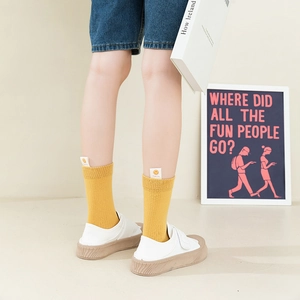 Bright yellow mid-calf socks with smiley face tag worn with white canvas shoes