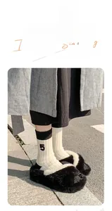 Detail of cream ribbed socks with a black number 5 patch worn with black plush slippers