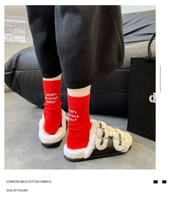 Detail showing red cotton socks with white lettering print and plush slippers on feet