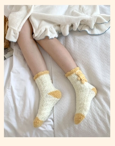 Gros plan de chaussettes en polaire corail avec nœud jaune sur literie blanche