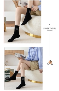 Detailed view of black ribbed crew socks with white embroidered smiley face on the ankle