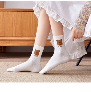 Detail of white cotton sock featuring a brown bear embroidery and ribbed cuff texture