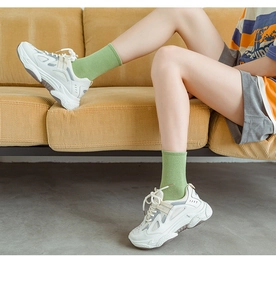Close-up of white chunky sneakers worn with green crew socks on a yellow sofa background