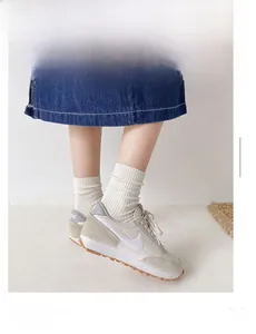 Detail of white cotton crew socks paired with beige sneakers and a denim skirt