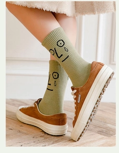Close-up of grass green cotton mid-tube socks with funny cartoon face design and brown sneakers