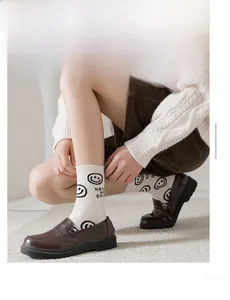 Détail de chaussettes en coton avec smiley et texte portées avec des mocassins bruns