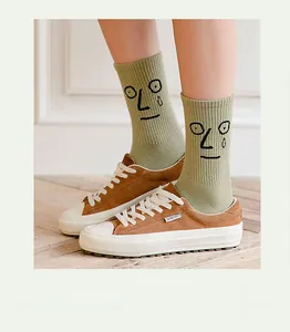 Detail of green cotton mid-calf socks with grumpy face embroidery and brown suede shoes