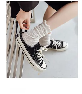 Detail of white lace jacquard socks paired with black canvas mule sneakers