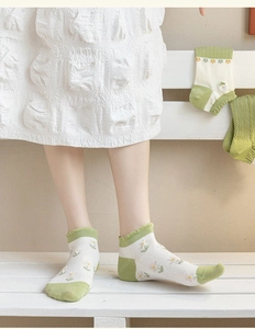 Detailed close-up of white women's ankle socks with green daisy patterns and frilly edges