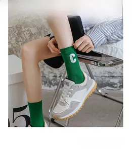 Close-up of bright green cotton socks with white letter C embroidery and retro sneakers