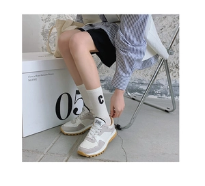 Detail of white cotton crew socks with black C letter embroidery worn with retro sneakers