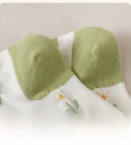 Detail of reinforced green heel and small daisy embroidery on white cotton ankle socks