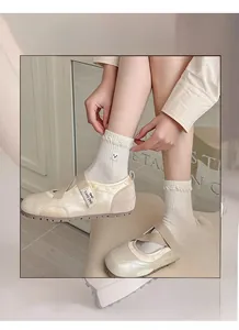 Detail of cream ballet flats with crisscross straps and white socks featuring bear embroidery