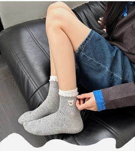 Close-up of light gray socks featuring cute bear embroidery and white ruffled edges