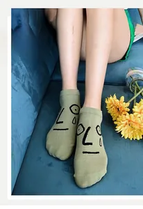 Close-up of light green cotton socks with abstract black line face pattern on blue sofa