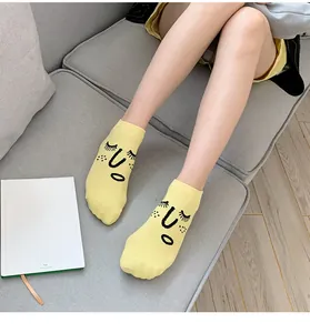 Detail of yellow cotton ankle socks with playful cartoon face design on model feet