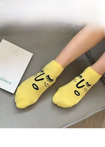 Close-up of bright yellow cotton socks with funny cartoon face patterns on a grey sofa