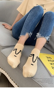 Close-up of beige cotton socks featuring minimalist black abstract face embroidery detail