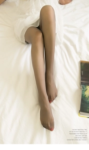 Detail of ultra-thin velvet sheer tights on legs against white bedding lifestyle backdrop