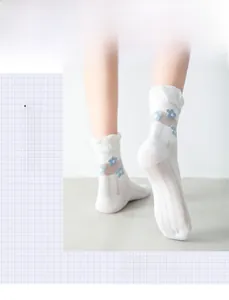 Detail of white mesh mid-calf socks featuring blue 3D flower embroidery and ruffle trim