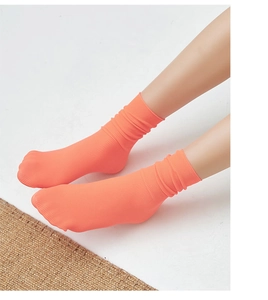 Detail view of bright orange ribbed velvet slouch socks with vertical stripe texture