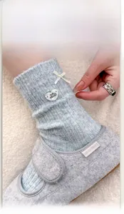 Detail of light blue wool blend sock with white ribbon bow and heart-shaped charm decor