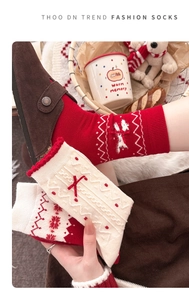 Detail von roten Weihnachts-Wollsocken mit Schleife, Plüschbommeln und Strickmustern