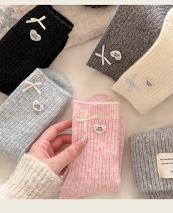 Close-up of wool socks featuring cute bow details and heart-shaped logo pendants