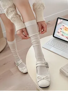 Close-up of white silk knee-high slouch socks paired with Mary Jane shoes on wood floor