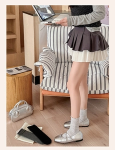 Detail of grey ruffled crew socks paired with silver Mary Jane shoes and pleated skirt