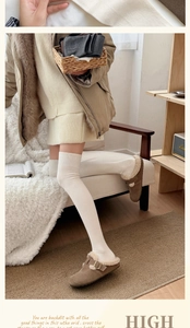 Detail of cream cable knit over-the-knee socks paired with brown fuzzy slippers