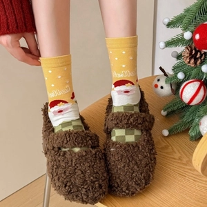 Brown plush Mary Jane slippers paired with yellow Christmas Santa socks in warm holiday setting