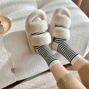 Plush cream faux fur slippers with double straps worn over striped cashmere crew socks