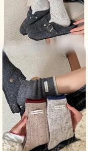 Close-up of wool socks with Wishing you luck label and grey felt mules on knit rug