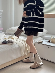 Gros plan d'un pull en maille rayé avec des chaussettes beiges et des chaussons fourrés