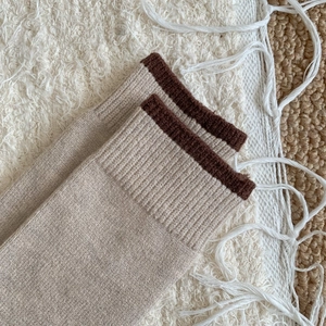 Détail de chaussettes mi-mollet en maille beige avec bord-côte contrasté marron