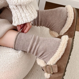 Brown ribbed crew socks with fuzzy suede mule shoes on a cozy lambskin chair