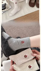 Detailed close-up of bear embroidery on thick rib-knit wool socks in neutral tones