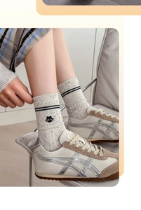 Close-up of beige knit crew sock with speckled yarn, cat embroidery, and retro sneakers