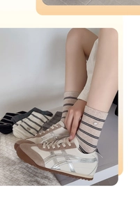Close-up of beige sneakers with silver stripes and khaki striped cotton crew socks
