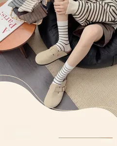 Détail de chaussettes à rayures avec des sabots en daim beige sur sol en bois