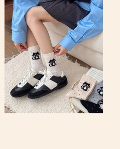 Detailed view of white cotton socks featuring cute cartoon cat with red hat and bow details