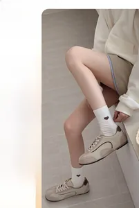 Gros plan de chaussettes blanches avec broderie cœur brun et baskets beige