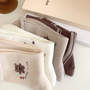 Gros plan de quatre paires de chaussettes tons terre avec broderie ours et texte