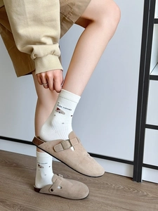 Détail de sabots en daim beige portés avec des chaussettes à motif d'ours