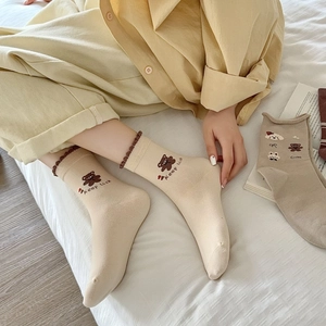 Détail de chaussette en coton beige avec bord à volants marron et motif ours brodé
