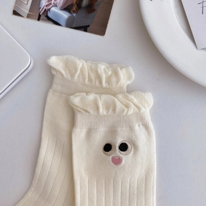 Detail of white cotton socks featuring frill cuffs and cute cartoon face embroidery