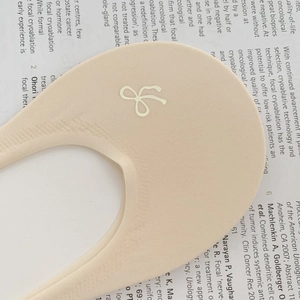 Detail of skin-tone invisible liner sock with bow logo on a vintage newspaper