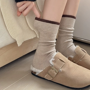 Close-up of beige knit socks with contrast dark brown cuffs worn with cozy slippers