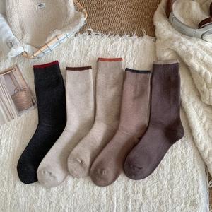 Detailed view of 5 pairs of winter crew socks in earth tones laid on a white fringed rug